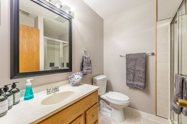 A bathroom with a white sink, wooden vanity, a large mirror, a toilet, and a glass shower enclosure.