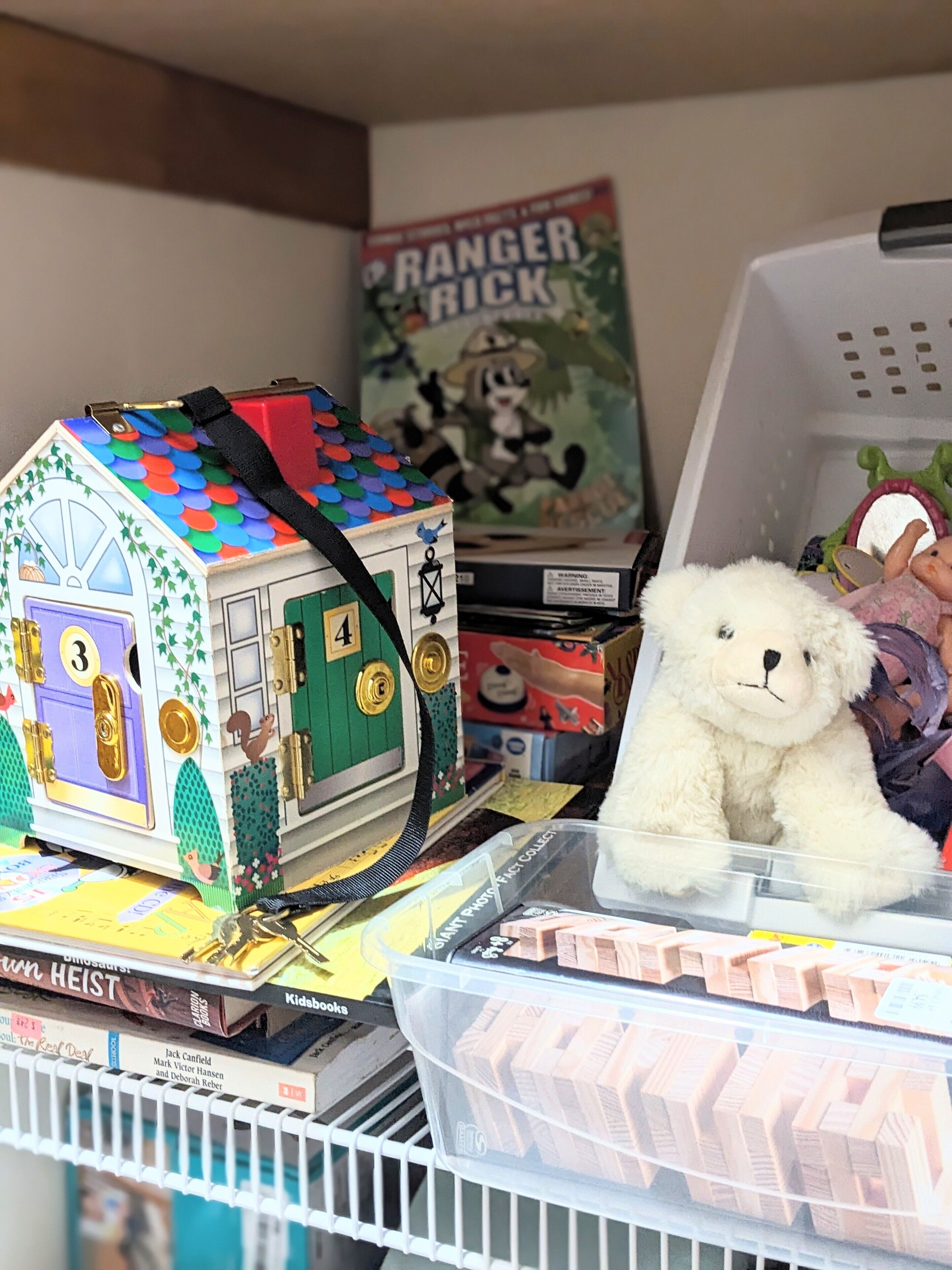 Una repisa con una maqueta de una casa, un oso de peluche y varios libros.