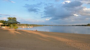 Una spiaggia con un ombrellone verde, barche e un lago tranquillo.