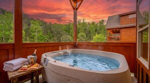 A hot tub with a wooden deck, a table with snacks and drinks, and a view of a forested area. - Rustic Mountain Retreat by Ghosal Luxury Lodging (Sevierville)
