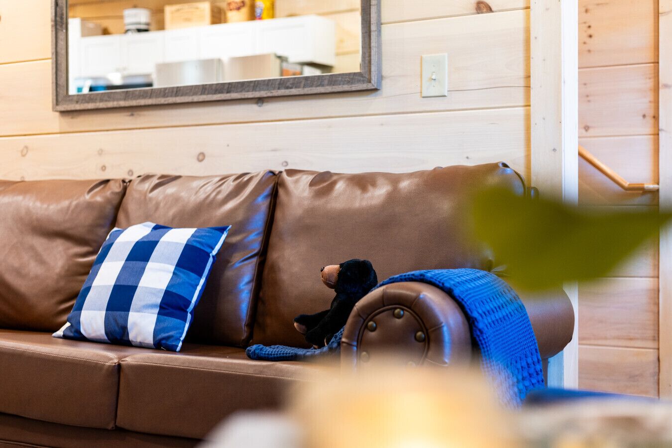 A brown leather sofa with a blue and white checkered pillow and a knitted blanket.