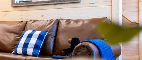 A brown leather sofa with a blue and white checkered pillow and a knitted blanket.