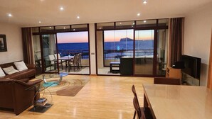 Een ruime woonkamer met een grote glazen deur die uitkomt op een balkon met uitzicht op zee.