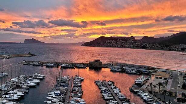 Een jachthaven met aangemeerde boten, een haven en een stadsgezicht met bergen op de achtergrond.