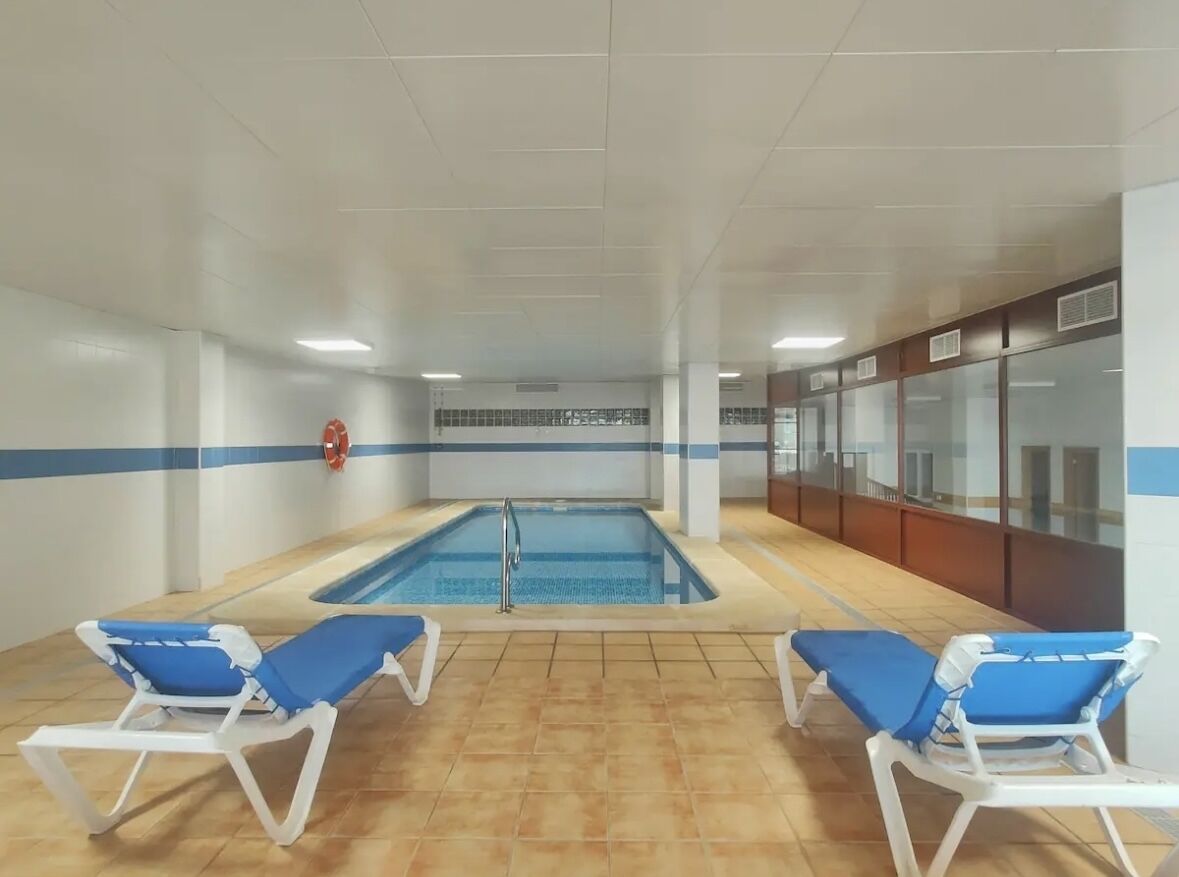 Una piscina interior con dos sillas reclinables azules y un extintor en la pared.