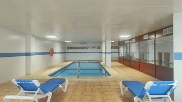 Una piscina interior con dos sillas reclinables azules y un extintor en la pared.