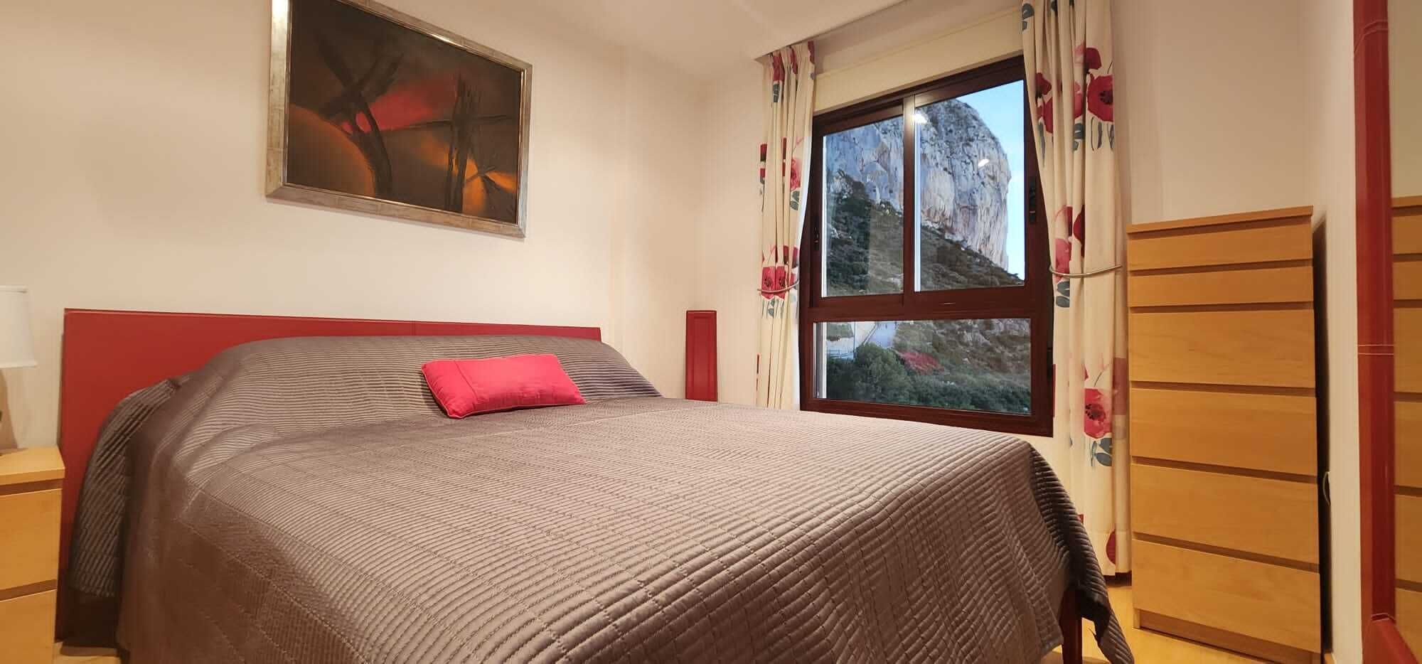 Une chambre à coucher avec un lit, un tableau au mur, une fenêtre avec des rideaux et une armoire.