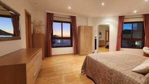 Een slaapkamer met een groot bed, een houten dressoir en uitzicht op zee.