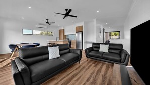 Un salon moderne avec deux canapés en cuir noir, un plancher en bois et un ventilateur de plafond.