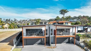 Une maison moderne à deux étages, dotée d’un garage, de grandes fenêtres et d’un toit plat.