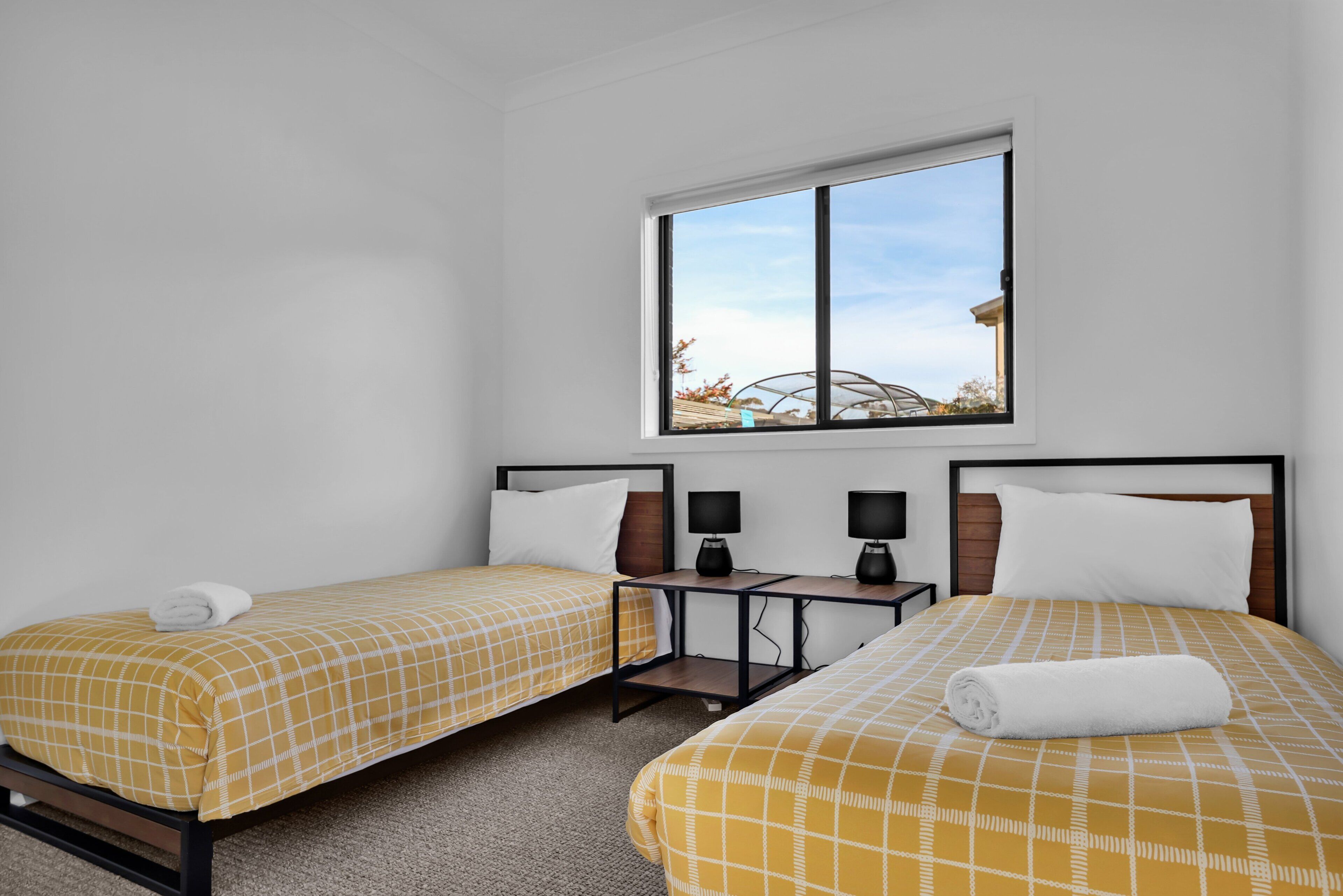 A hotel room with two single beds, a small table with two lamps, and a window with a view of a greenhouse.