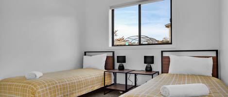 A hotel room with two single beds, a small table with two lamps, and a window with a view of a greenhouse.