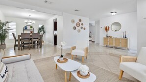 Un salón amplio con comedor, un sofá blanco, una mesa de centro y un mueble con objetos decorativos.