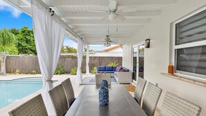 Un patio techado con piscina, mobiliario exterior y ventilador de techo.