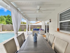 Eine überdachte Terrasse mit Pool, Gartenmöbeln und Deckenventilator.