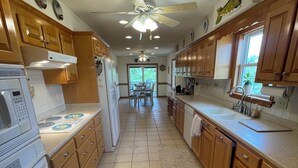 A kitchen with wooden cabinets, a microwave, a stove, and a ceiling fan. - Beachside Breeze! 5 BR 3 BA beach paradise!  (Nags Head)