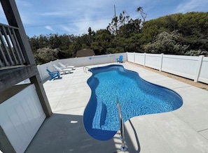 Une piscine entourée d’une clôture blanche, avec des chaises longues et une terrasse en bois.