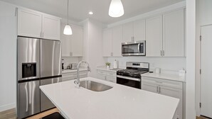 A modern kitchen with white cabinetry, stainless steel appliances, and pendant lighting.
