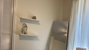 Ein ordentlich bezogenes Bett mit aufgerollten Handtüchern, einem Spiegel und einem Regal mit Dekoration in einem Hotelzimmer.