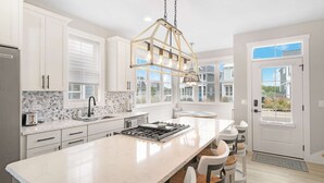 A modern kitchen with white cabinetry, a central island, a gas stove, and a hanging light fixture. - Sit, Stay, Relax | Welcome to Serendipity (Ottawa)
