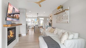 A modern living room with a fireplace, a television, a wooden ceiling fan, and a white sofa. - Sit, Stay, Relax | Welcome to Serendipity (Ottawa)