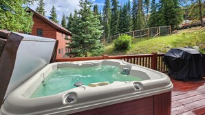 A hot tub on a wooden deck with a view of a forest and a building in the background. - Mountain Retreat with Deck and Hot Tub (Blue River)