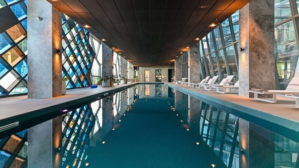 Une piscine intérieure aux parois en verre transparent, dotée de chaises longues et présentant un design architectural moderne.