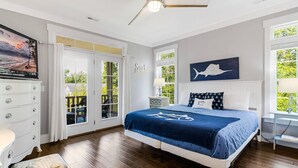 A bedroom with a large bed, a ceiling fan, a TV, and a view of the outdoors.