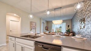 Una cucina moderna con un'ampia isola, mobili bianchi e illuminazione a sospensione.