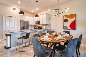 A modern kitchen with white cabinets, a central island, and a dining area with a round table and chairs.
