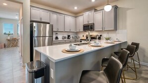 Una cucina moderna con elettrodomestici in acciaio inossidabile, un'isola centrale con sgabelli da bar e una lampada a sospensione luminosa.