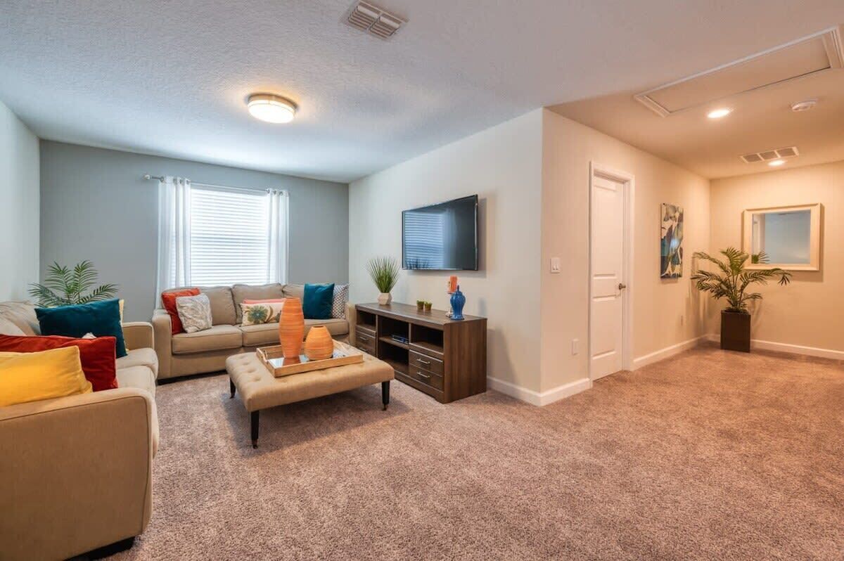 A living room with a sofa, ottoman, entertainment center, and a flat-screen TV mounted on the wall.