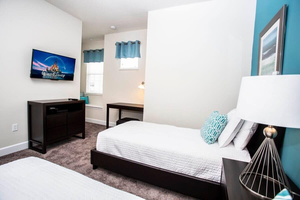 A bedroom with a bed, a desk, a TV, and a lamp.