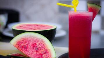 A glass of red beverage with a yellow straw and a slice of watermelon on the rim.