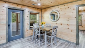 L’intérieur d’un chalet en bois, avec une table à manger, des chaises, un miroir et une porte.