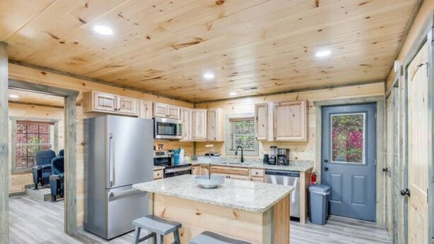 Une cuisine spacieuse avec des meubles en bois, un îlot central en granit doté de tabourets et un réfrigérateur.