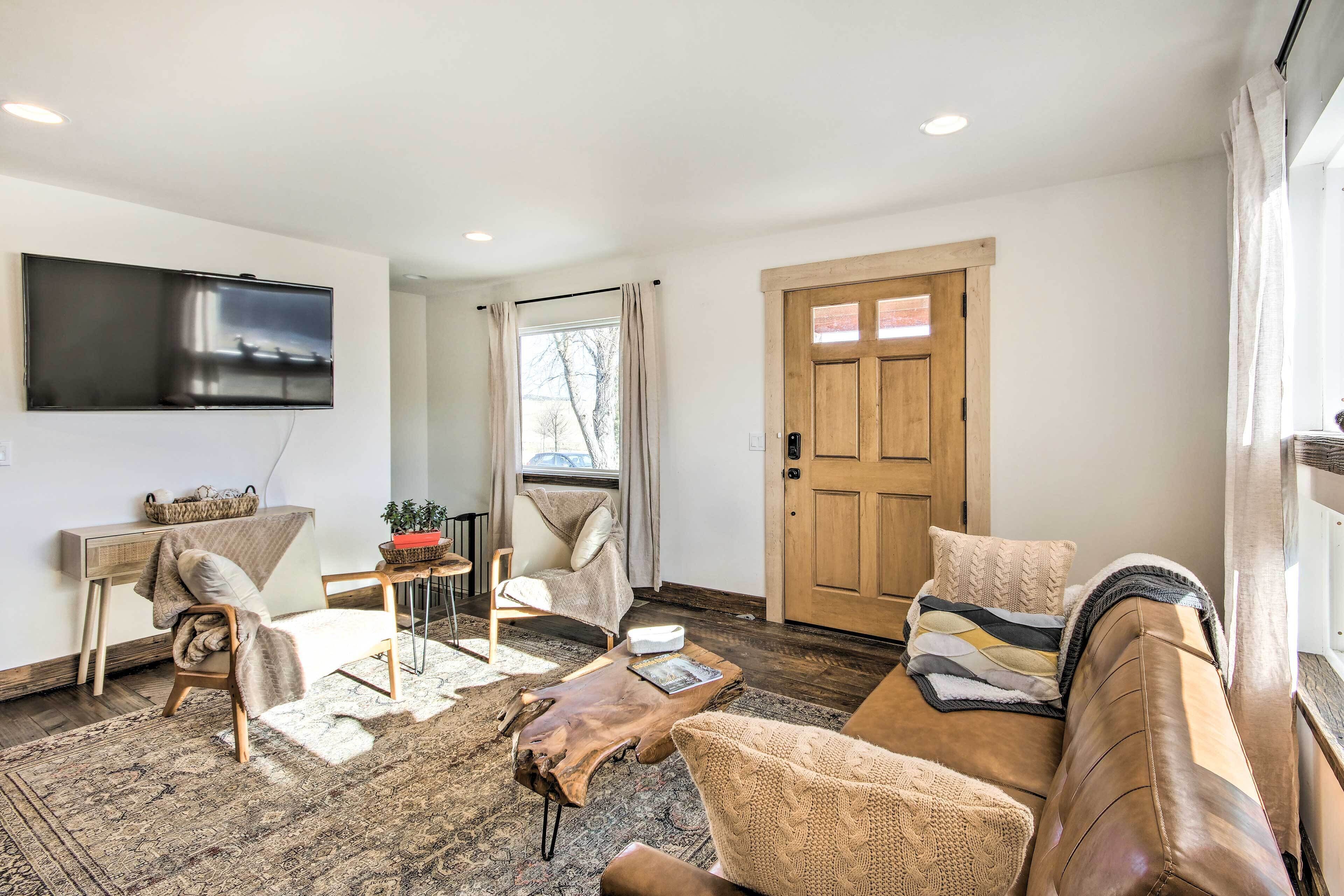A living room with a sofa, armchair, coffee table, and a TV mounted on the wall.