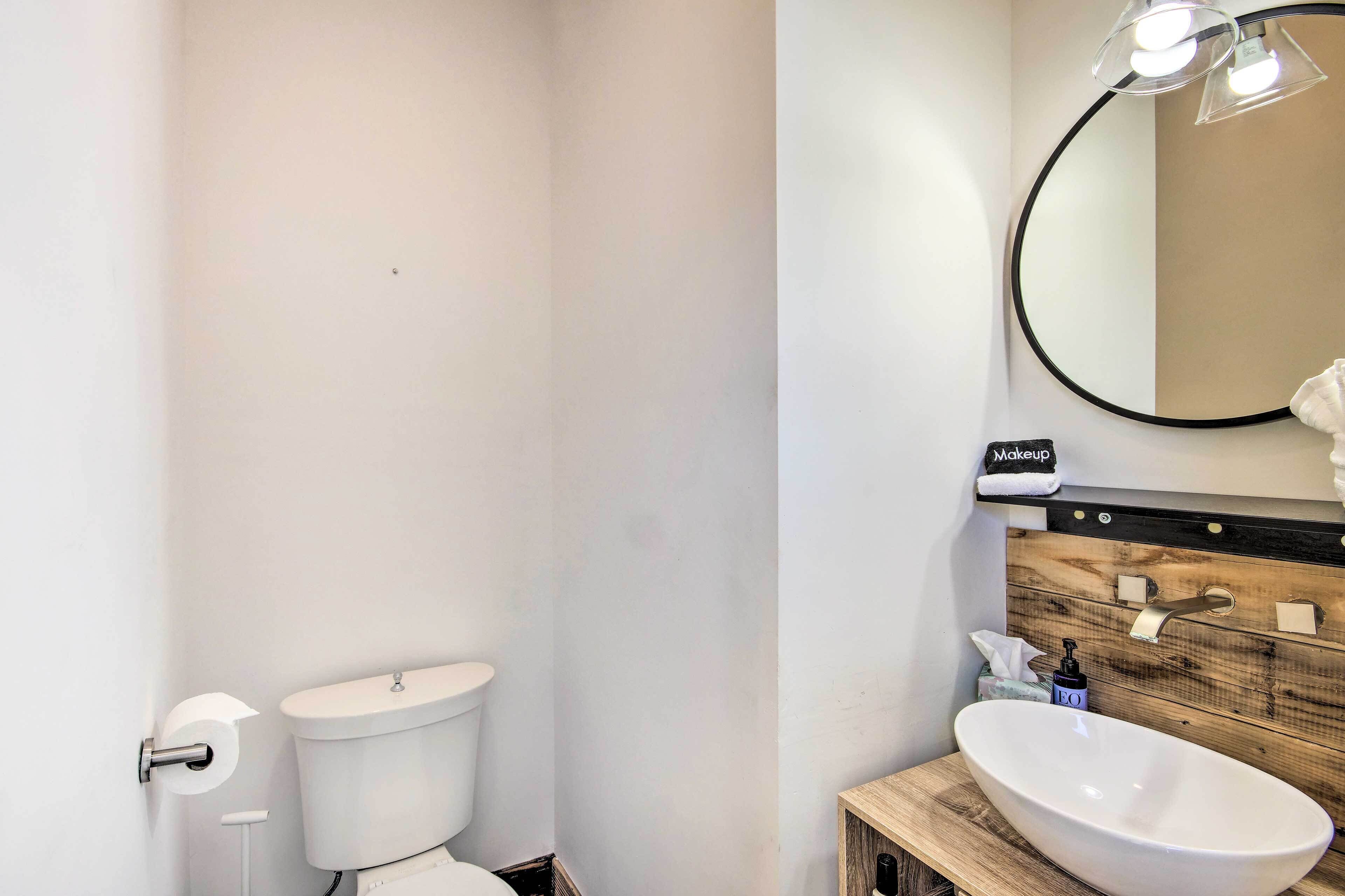 Ein Badezimmer mit einer weißen Toilette, einem Holzkosmetikschrank mit Waschbecken und einem Spiegel darüber.