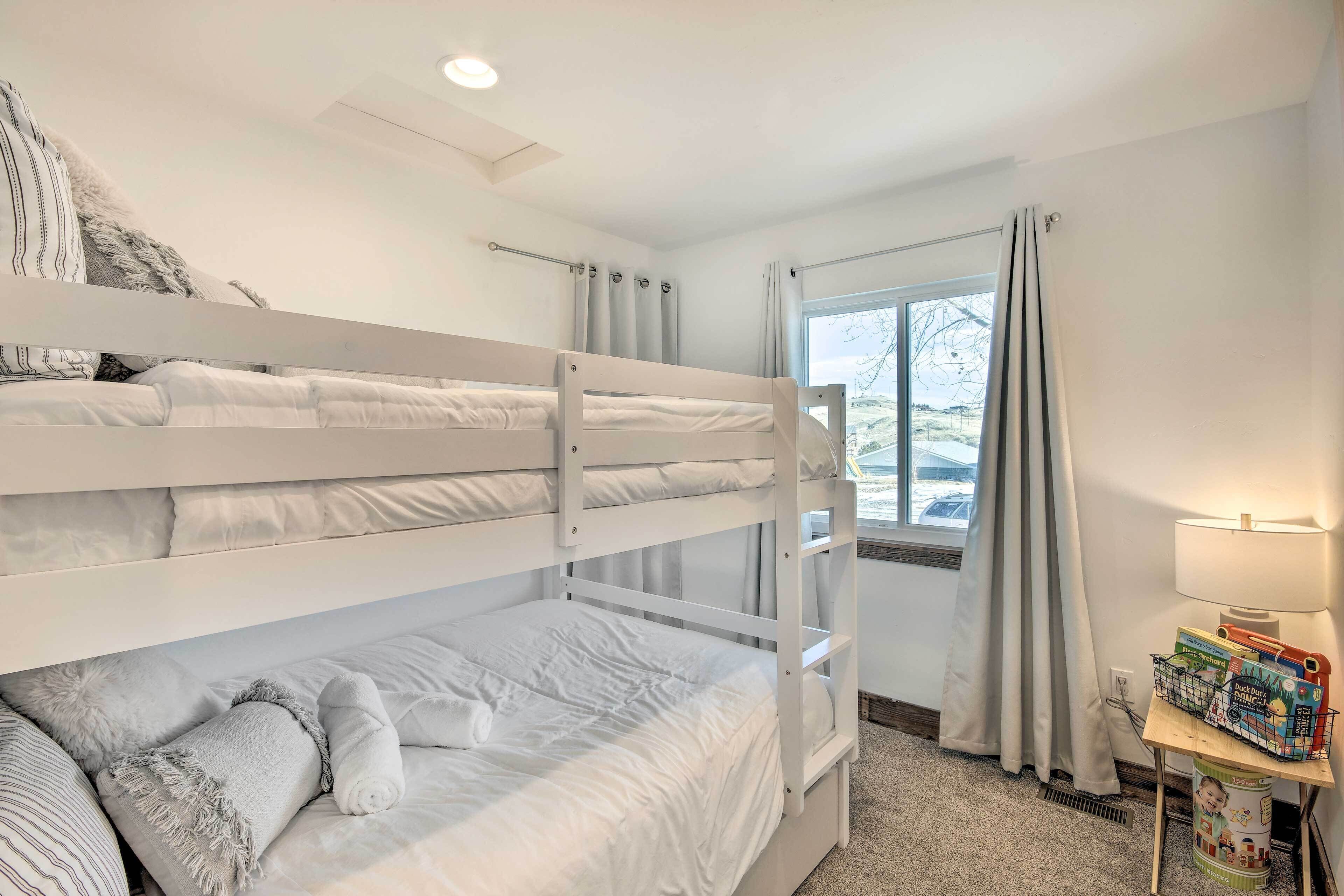 Een slaapkamer met een stapelbed, een raam, een lamp en een klein tafeltje met kinderspeelgoed.