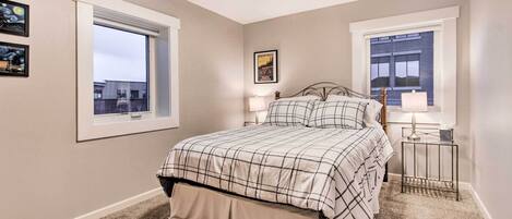 A bedroom with a bed, two bedside tables, a window, and a picture on the wall.