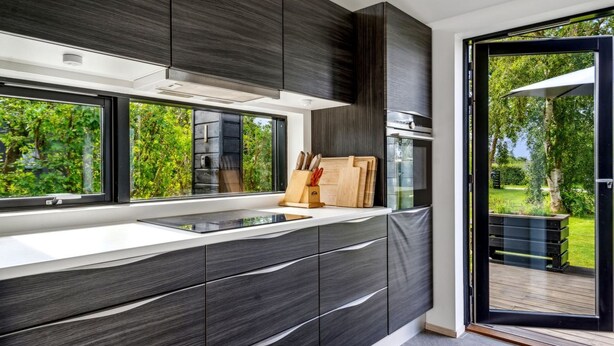 Een moderne keuken met donkere houtkasten, een groot raam en uitzicht op een tuin.