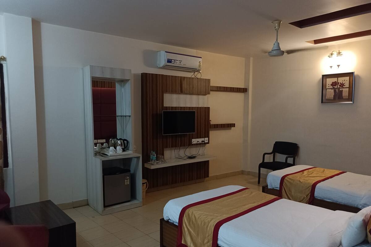 A hotel room with two beds, a desk with a flat-screen TV, an air conditioner, and a ceiling fan.