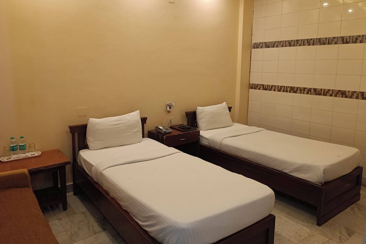 A hotel room with two single beds, a small table with a phone and a bottle, and a wall with a patterned tile design.