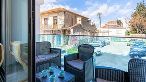 A balcony with wicker furniture and a table, overlooking a parking area and buildings.