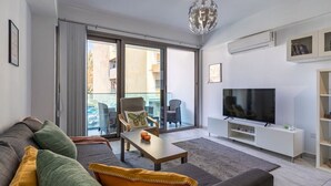 A modern living room with a sofa, coffee table, TV, and a balcony with chairs.