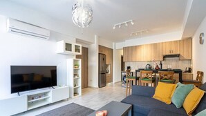 A modern living room with a flat-screen TV, a sofa with cushions, a coffee table, and a chandelier.