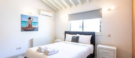 A bedroom with a bed, a nightstand, a window, a radiator, and a painting on the wall.