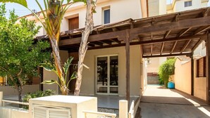 Un'area esterna coperta con una pergola in legno, una palma e un edificio con tetto in tegole.