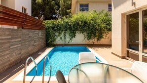 Una piscina con un solarium in legno, un tavolo in vetro e una sedia.