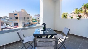 A balcony with a table and chairs, a lantern, and a view of buildings and cars. - Kmeidos 1-Bedroom Apartment & Balcony in Larnaca (Cyprus - Larnaca)